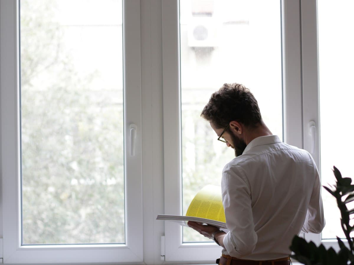 An inspector with a hard hat and clipboard checking notes by a window