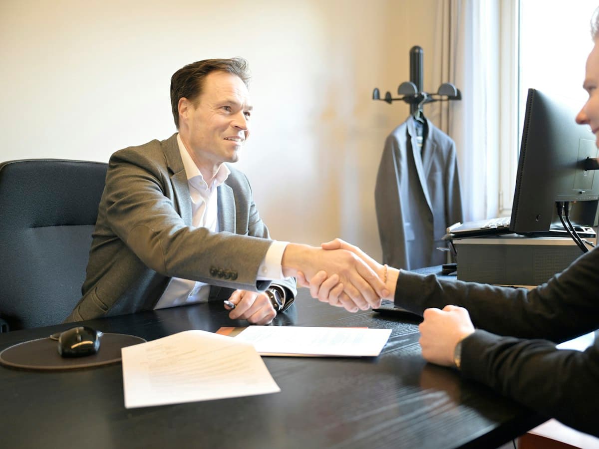 Two people shaking hands across a desk over signed papers