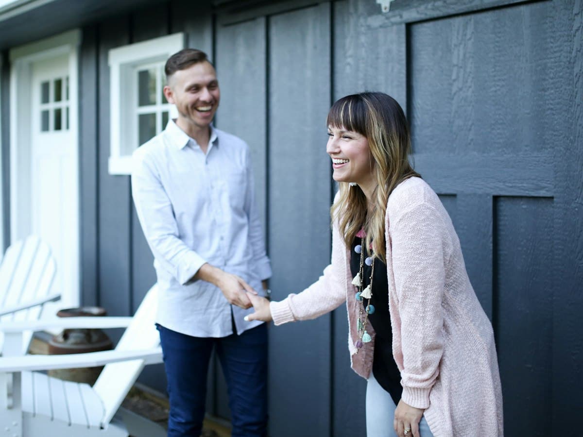 A homeowner shaking hands with a visitor outside a weatherboard house